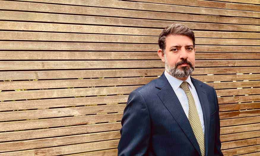 An academic in suit standing next to a wall. 