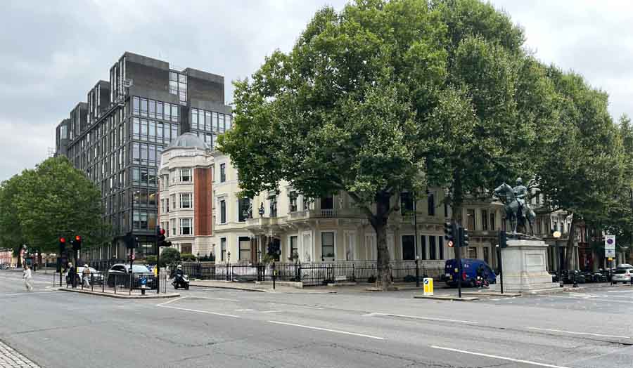 Street corner featuring modern and classic buildings with trees and a monument in foreground 