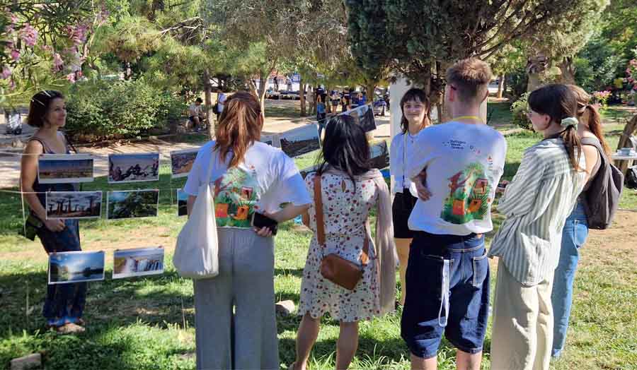 View of people next to photographs hanging on a washing line, with a park context in the background