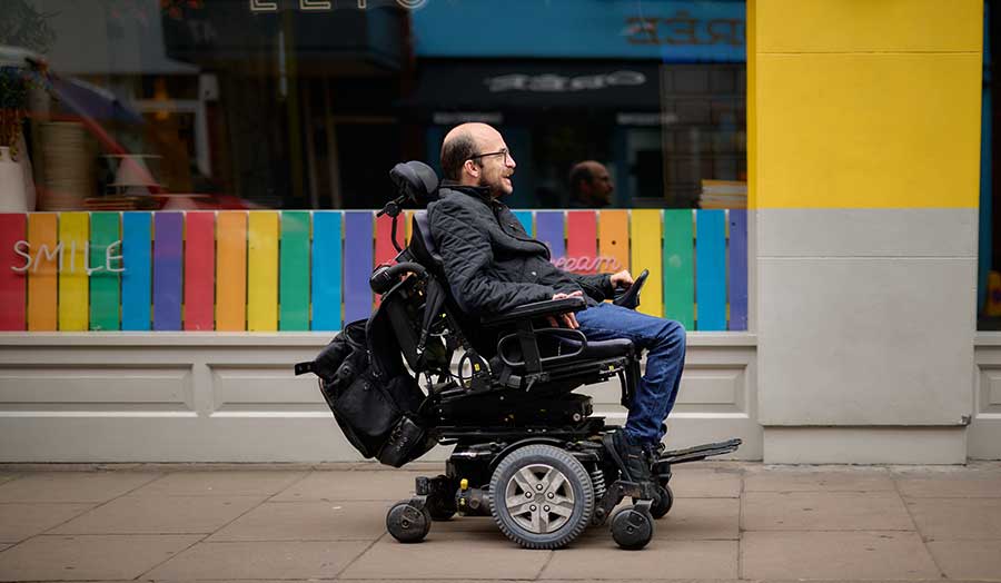 Josh pictured in his wheelchair whizzing past a rainbow shop display in Soho with the word 'smile' on it