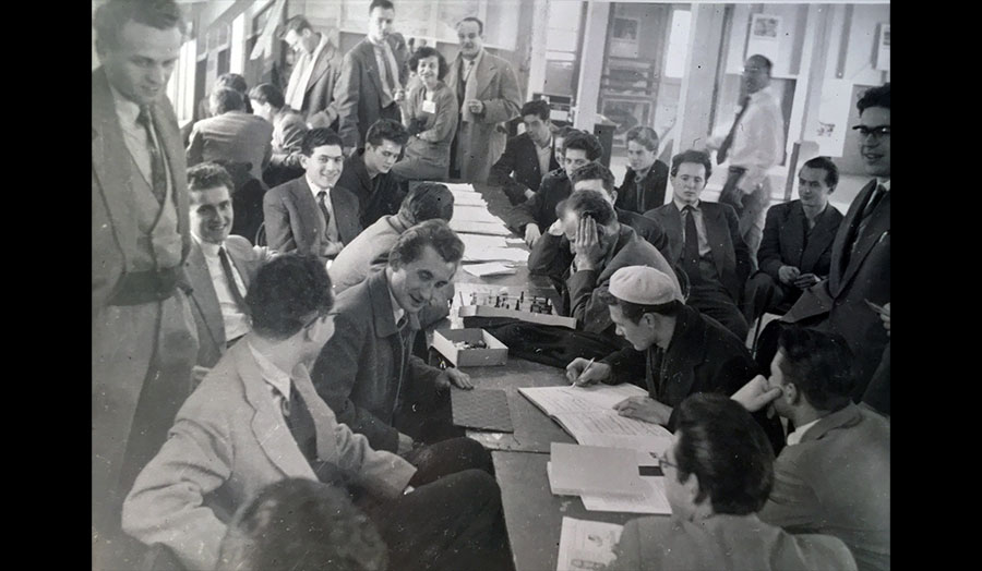 A 1956 black and white photograph of a large group of people around a table 