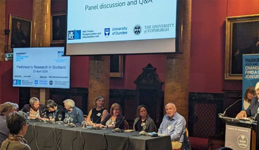 Seven people sit in front of an audience for a panel discussion at a conference