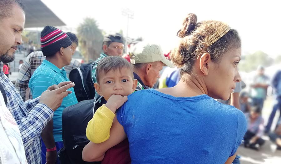 A woman in a crowd holds a child, who looks directly at the camera