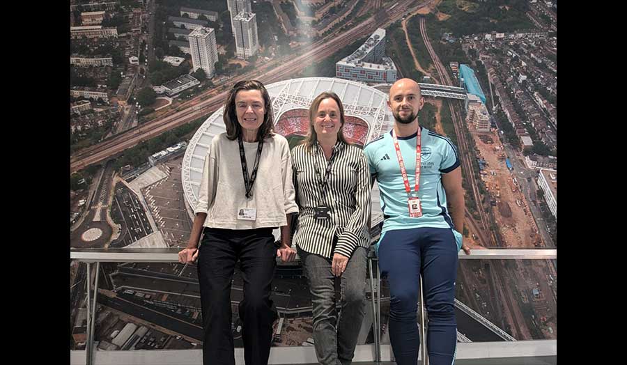 Three people stand in front of a large photograph of the Arsenal Stadium