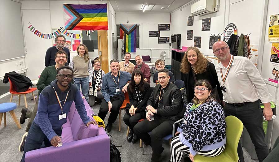 A group of people in a room decorated with a rainbow Pride flag