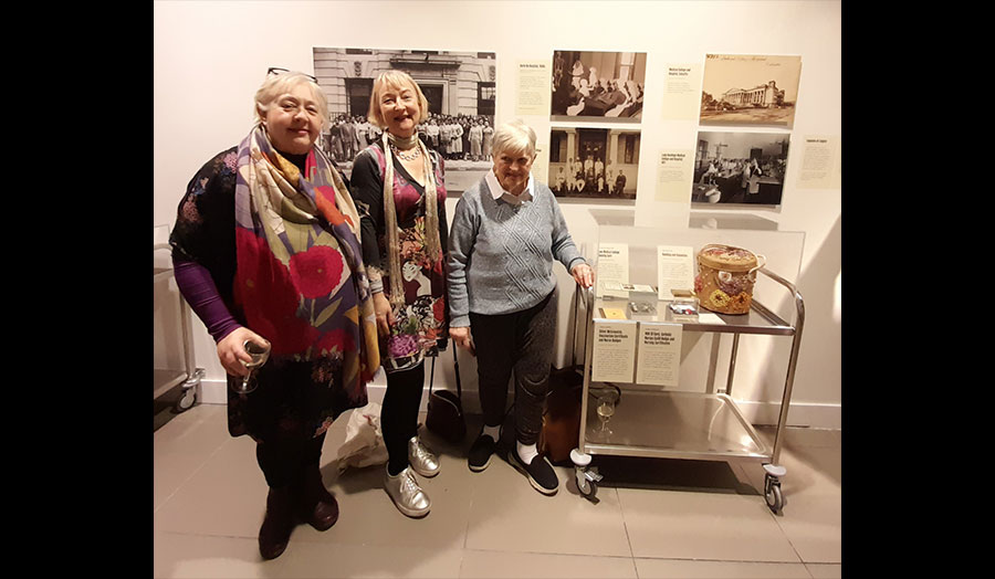 Three people stand in front of displayed photographs and personal items at a museum exhibition