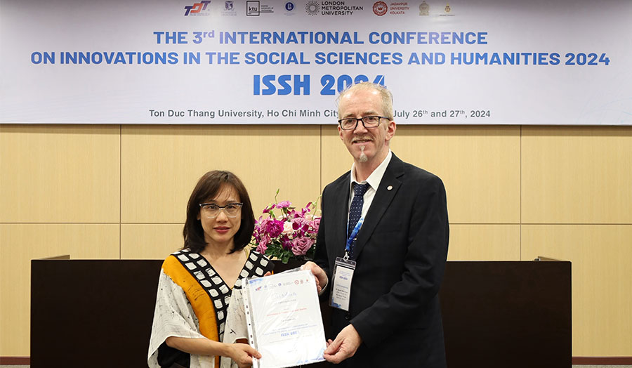 Two people stand in front of a conference banner, holding a document together