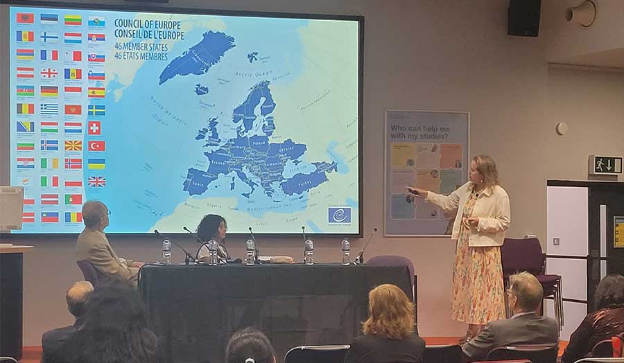 Keynote speaker Sarah Keating presents to an audience in front of a map of Europe