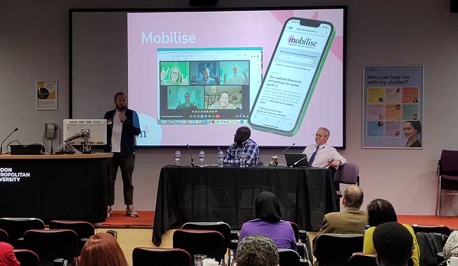 A man presents to an audience, standing in front of a screen showing the title 'Mobilise'