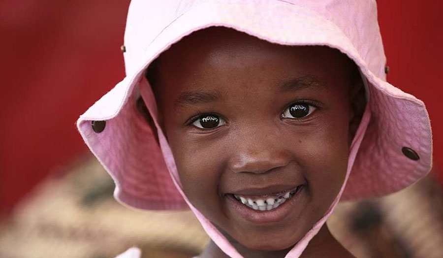 A child in a pink hat smiles at the camera