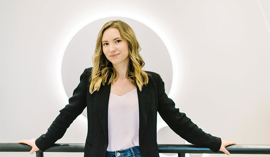 Olka pictured smiling in a suit with contemporary lighting behind her